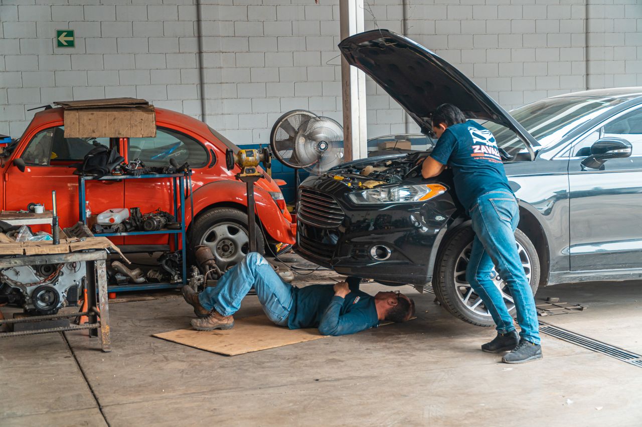 Mechanics working in an automotive workshop, repairing cars and performing maintenance.